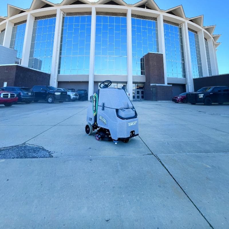 Tomcat Stand On Floor Scrubbers Rival event venues concrete A Tomcat Rival stand on battery floor scrubber is  cleaning the concrete sidewalks af a concert and entertainment  venue.